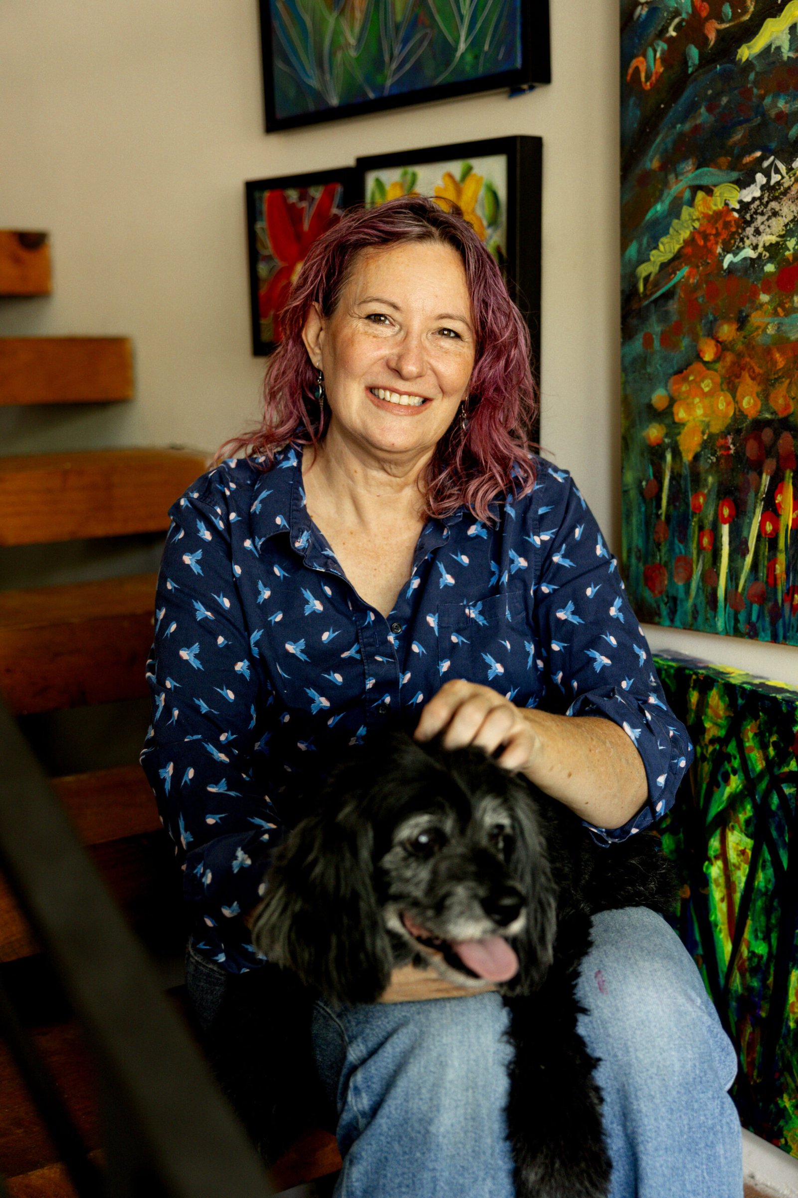Artist Lee Suzanne Jordan sitting with her dog molly in front of a few of her paintings
